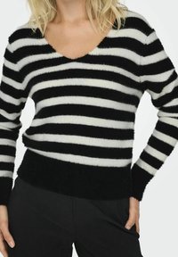 Pull à rayures noires et blanches avec un col en V profond, texture duveteuse, manches longues et taille ajustée. Le tissu semble doux et chaud.