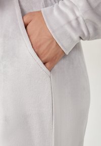 Lichtgrijze fleece hoodie met een zijzak. De textuur is soepel, met een licht verhoogde pool, en de manchetten zijn aansluitend.