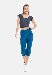 Top corto gris y pantalones capri azul con cintura elástica. Los pantalones cuentan con bolsillos y pliegues. Modelo lleva zapatillas blancas.