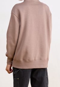 Överdimensionerad beige sweatshirt med rund halsringning och ribbade manschetter och fåll. Mjuk textur, minimal sömdetalj på baksidan.