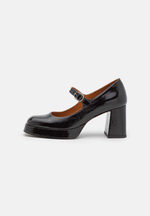 Schwarzer Mary Jane Schuh aus Lackleder mit abgerundeter Spitze, verstellbarem Schnallenriemen, klobigem Blockabsatz und Plateau-Sohle auf weißem Hintergrund.