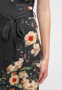 Vestido floral con una tela negra decorada con flores en tonos pastel y detalles en verde. Incluye un cinturón atado de la misma tela.