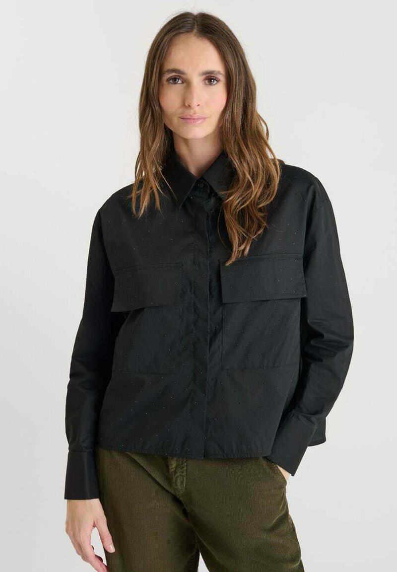 Black long-sleeve shirt with a structured collar, two large chest pockets, and subtle texture, paired with green corduroy pants.