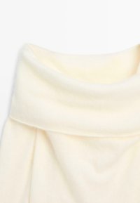 Tissu crème, doux, avec un col replié. La texture est lisse, présentant un drapé léger et des détails de couture subtils.