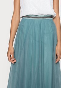 Vaaleansininen tyllihame, jossa on kerrottu vyötärö ja metallinhohtoinen hopea yksityiskohta. Materiaali on pehmeä ja ilmava.