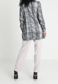 Tunika a maniche lunghe con motivo serpente, caratterizzata da un orlo lungo, abbinata a pantaloni chiari e stivaletti neri con tacco alto.