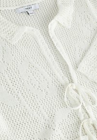 Cardigan blanc en maille avec motif dentelle, fermeture à nouer devant et étiquette de marque "NEXT" à l'intérieur du col.