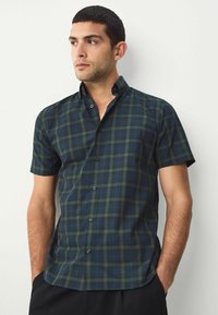 Košeľa s krátkym rukávom v tmavozelenej a námorníckej plaid vzore, s golierom na gombíky a jemnou textúrou, vyrobená z ľahkého materiálu.