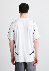 White athletic shirt with black accents and stripes. Short sleeves and a round neckline. Smooth texture, lightweight fabric.