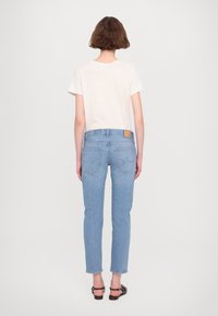 Jasnobeżowy t-shirt z krótkim rękawem w połączeniu z dopasowanymi, jasnoniebieskimi dżinsami, wyposażonymi w tylne kieszenie oraz skórzaną metkę na pasku talii.