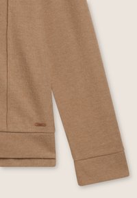 Pull en maille côtelée marron clair, avec une coupe décontractée et des manches à revers. Présente une petite étiquette marron sur l'ourlet, avec un détail de tissu texturé visible.