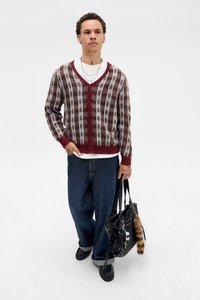 Burgunderfarget og hvit rutet cardigan, med knapper foran, i ullblanding. Løse lyseblå denimbukser, svart håndveske med pelsdetalj, svarte sko.