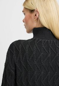 Schwarzer Rollkragenpullover aus Kabelstrick mit einem strukturierten Diamantmuster und einem gerippten Kragen. Der Stoff wirkt dick und gemütlich.