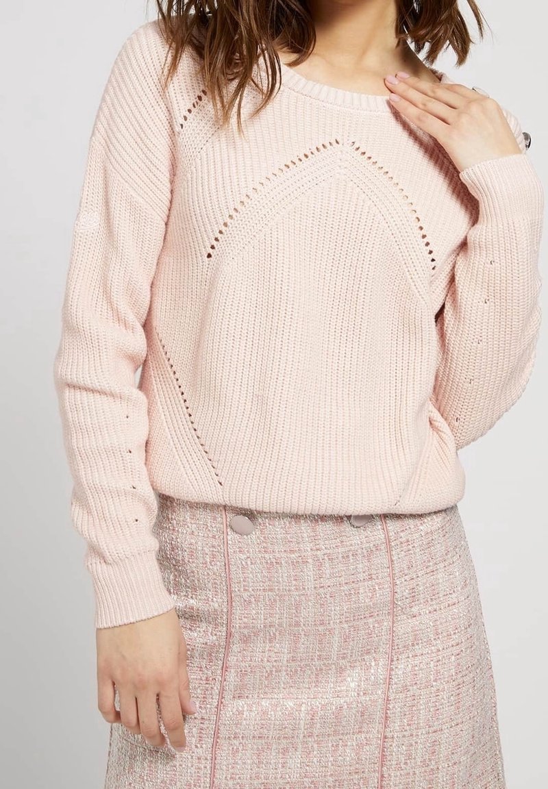 Pull rose clair en maille avec un motif texturé, présentant un motif ajouré. Porté avec une jupe ajustée rose et argentée à motif, ornée de boutons.
