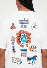 Balta marškinėliai su spalvingais animaciniais grafikais, įskaitant Nike logotipą, plytas, saugos kūgį ir įvairius linksmus elementus.