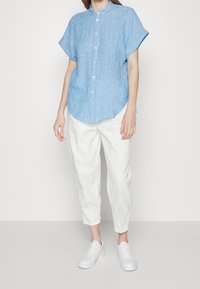 Ljusblå kortärmad skjorta med vita vertikala ränder, i kombination med lösa vita byxor och vita sneakers.