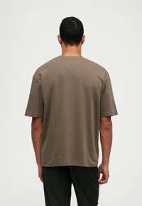 Καφέ κοντομάνικο t-shirt από μαλακό βαμβάκι με άνετη εφαρμογή. Λείος υφασμάτινος χαρακτήρας, στρογγυλή λαιμόκοψη και καθαρός σχεδιασμός χωρίς διακοσμητικά στοιχεία.