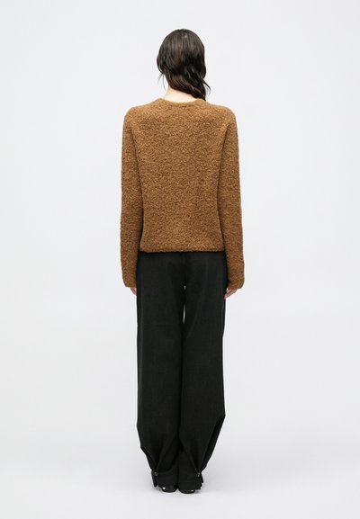 Brązowy sweter o fakturze z długimi rękawami, zestawiony z luźnymi czarnymi spodniami. Minimalistyczny design, bez widocznych wzorów ani elementów metalowych.