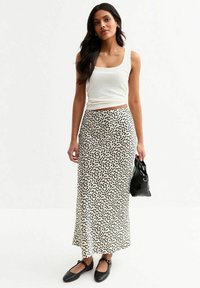 Witte geribbelde tanktop gecombineerd met een lange zwart-witte rok met stippen, platte zwarte schoenen en een kleine zwarte handtas. Glad textuur van de stof.