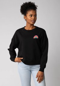 Zwarte sweatshirt met een ronde hals en een ontspannen pasvorm. Voorzien van een regenbooggrafiek en de tekst "WOMEN POWER" in levendige kleuren.
