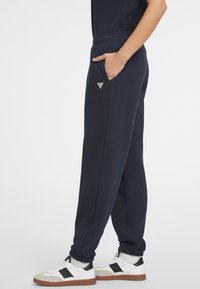 Navy sweatpants made of soft fabric, feature side pockets, elastic cuffs, and a small triangular logo patch on the left side.