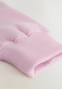 Różowy sweter dziewiarski przy mankiecie z teksturowanym ściągaczem i miękkim wykończeniem. Posiada zagięty brzeg dla dopasowanego fasonu. Brak widocznych wzorów lub metalowych elementów.