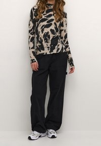 Haut beige à manches longues avec un imprimé abstrait noir, associé à un pantalon noir ample et des baskets grises. Tissu lisse et coupe décontractée.