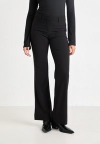 Black flared pants made of smooth fabric, featuring a tailored fit, belt loops, front pockets, and a clean silhouette with pressed seams.