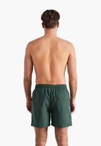 Shorts de bain verts avec une taille élastique, dotés d'une poche arrière. Texture lisse, coupe classique et longueur au genou.