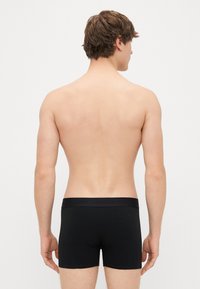 Sorte bomullsboxer med en glatt tekstur, med et merket elastisk midjebånd. Designet inkluderer en tettsittende form og dekning til midten av låret.