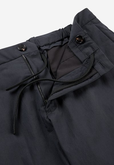 Black waterproof pants with a zip fly, adjustable drawstring at the waist, and two buttons, featuring smooth, lightweight fabric and subtle sheen.