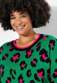 Strickpullover mit grüner Basis und schwarzem sowie pinkem Leopardenmuster, schwarzer gerippter Halsabschluss, weicher Textur und lockerer Passform.