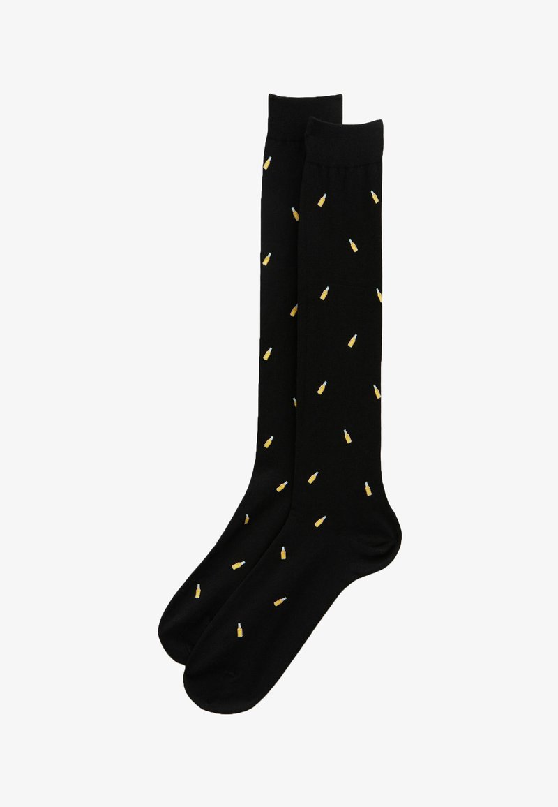 Chaussettes noires montant jusqu'aux genoux avec de petits motifs jaunes en forme de bouteilles de bière dispersés sur toute la surface.