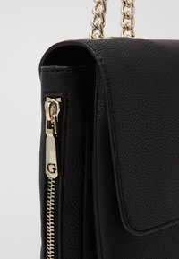 Borsa a mano nera in pelle con finitura testurizzata, accessori in oro e tracolla a catena. Caratterizzata da una chiusura con zip e un design a soffietto.