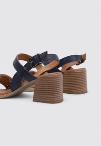 Sandalias de piel azul marino con tiras, con un tacón de bloque de madera redondeado, que cuentan con una hebilla de metal plateada y un diseño perforado en la plantilla.