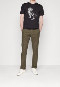 Czarny t-shirt z nadrukiem graficznym, oliwkowozielone spodnie i białe trampki. Codzienny krój o gładkiej fakturze i minimalistycznym designie.