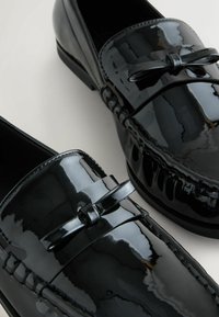 Sorte patenterede læder loafers med sløjfeaccent, mokkasin-sydekor, rund tå og lav hæl.