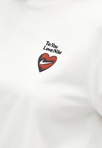 Λευκό ύφασμα με ένα μικρό κόκκινο και μαύρο γραφικό καρδιά που περιέχει ένα λευκό λογότυπο Nike και κείμενο που γράφει "Προς: Εσένα Αγαπώ: Nike".