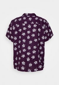 Camicia a maniche corte viola con bottoni e motivo a foglie bianche, vista da dietro su uno sfondo semplice.