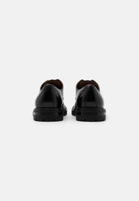 Chaussures en cuir noir avec une finition lisse, un talon rond et une semelle texturée. Dotées de coutures discrètes et d'un design classique.
