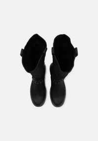 Botas de ante negras hasta la rodilla, con ojales redondos, detalle de costura y tiradores en la parte superior. Textura suave con una suela plana.