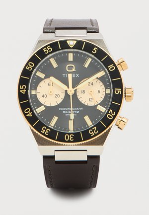 Ρολόι χρονόμετρο κουρδιστό Timex με μαύρο και χρυσό στεφάνι, δύο υποκαντράν κρεμ χρώματος, χρυσούς δείκτες και καφέ δερμάτινο λουρί.