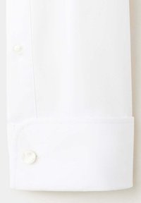 Poignet de chemise blanche avec un seul bouton blanc et une boutonnière visible sur un fond en tissu lisse.