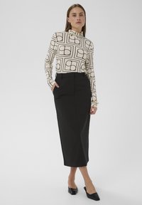 Langärmliges Rollkragenoberteil in Creme mit schwarzem geometrischem Muster, kombiniert mit einem schwarzen knielangen Bleistiftrock; schlankes Design. Schwarze Mules.