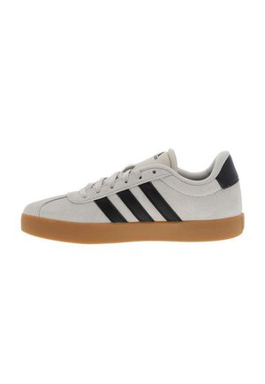 Zapatilla deportiva de corte bajo con parte superior de ante beige, tres rayas negras y tira en el talón, cordones blancos y suela de goma color caramelo.