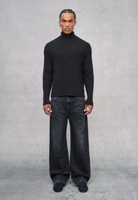 Suéter negro de punto con canalé y cuello alto, combinado con jeans de pierna ancha oscuros y calzado negro. Diseño simple y moderno sin patrones.