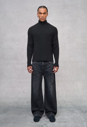Suéter negro de punto con canalé y cuello alto, combinado con jeans de pierna ancha oscuros y calzado negro. Diseño simple y moderno sin patrones.