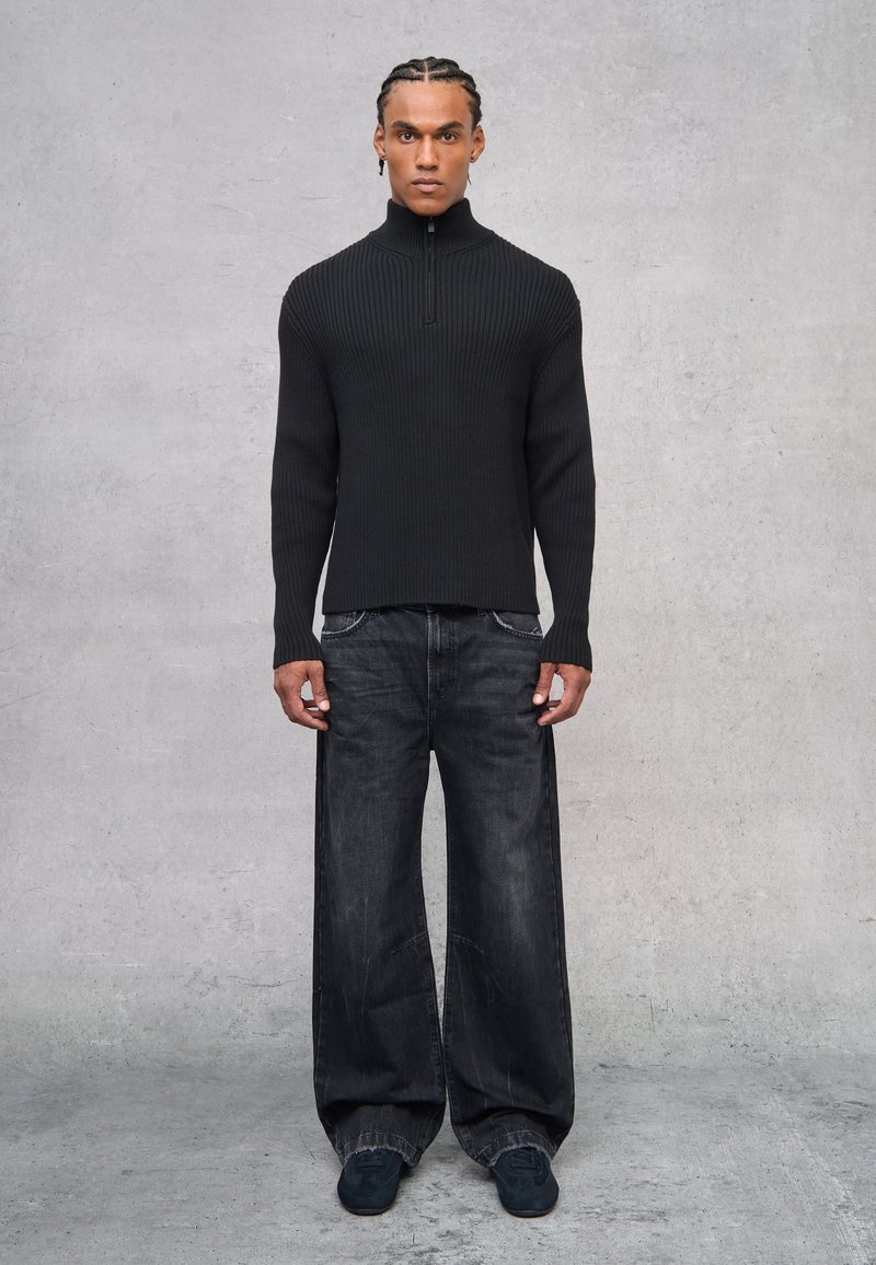 Suéter negro de punto con canalé y cuello alto, combinado con jeans de pierna ancha oscuros y calzado negro. Diseño simple y moderno sin patrones.