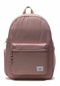 Sac à dos rose avec une texture de tissu lisse, une forme arrondie, une poignée supérieure, une poche zippée à l'avant, et une étiquette de marque brodée dans le coin inférieur droit.