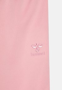 Jasnoróżowa tkanina z małym haftowanym logo Hummel, przedstawiającym stylizowane skrzydła pszczoły oraz tekst w prawym dolnym rogu.